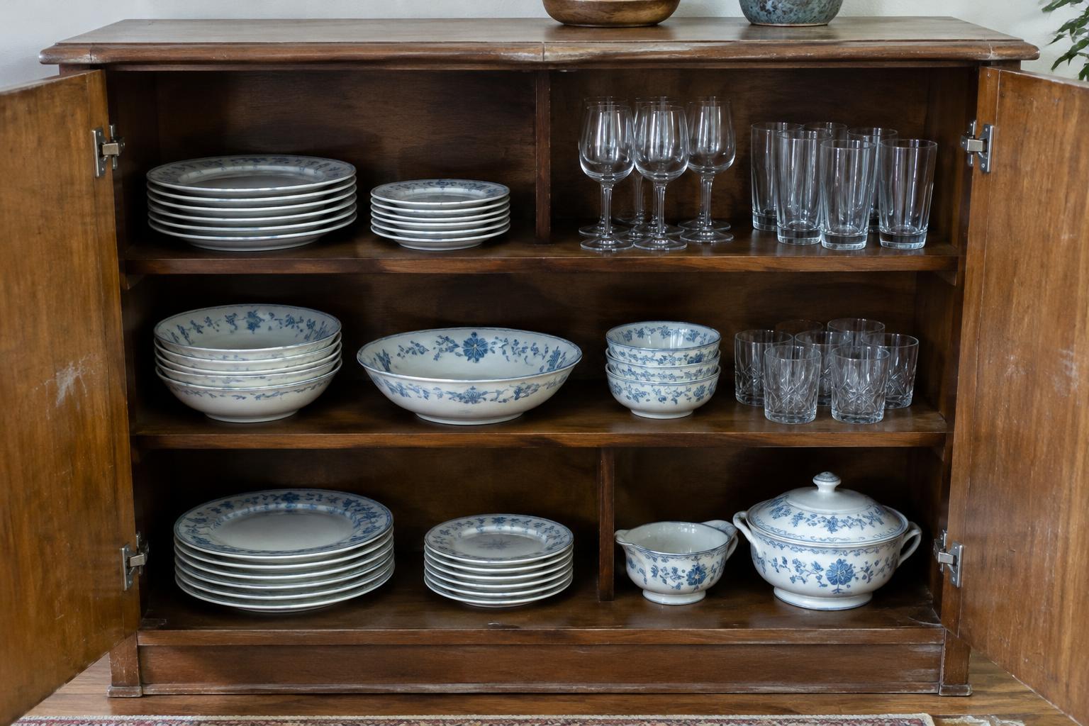 Open sideboard showing china, glassware and visible wear on the cabinet